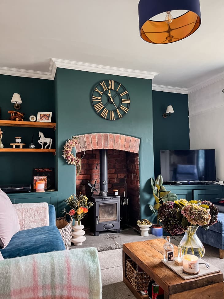 living room with one dark green accent wall, brick fireplace with black wood burning stove, and large clock above