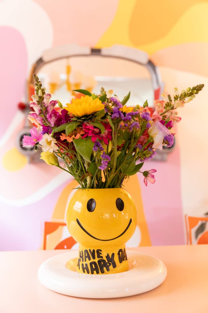 Smiley face vase filled with colorful floral arrangement.