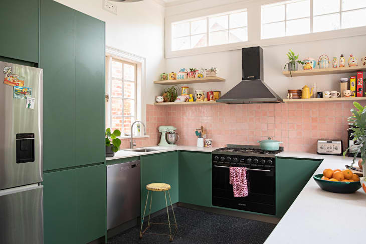 Pink tiles in kitchen with open shelves and green cabinets.