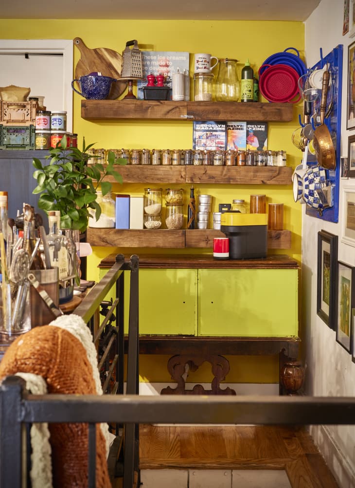 Spices line open shelves in yellow hued kitchen.
