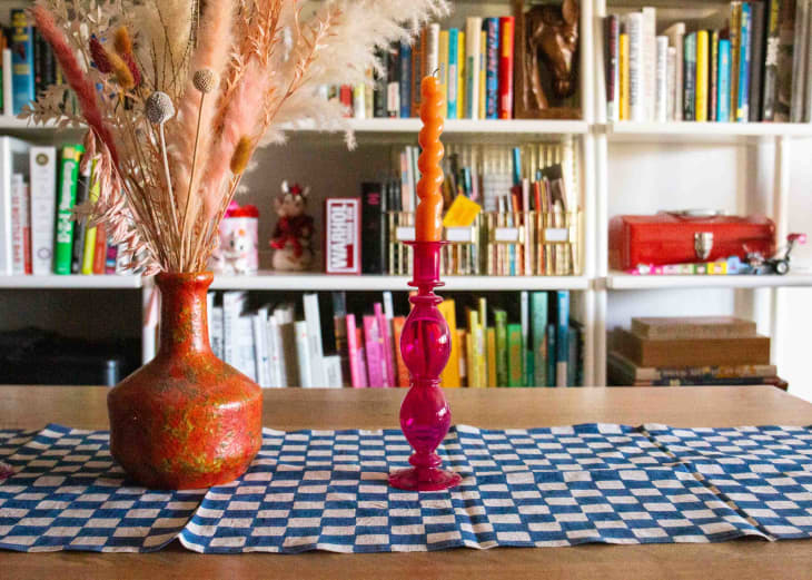 A pink vase with orange candle on a dining table in front of a bookcase.