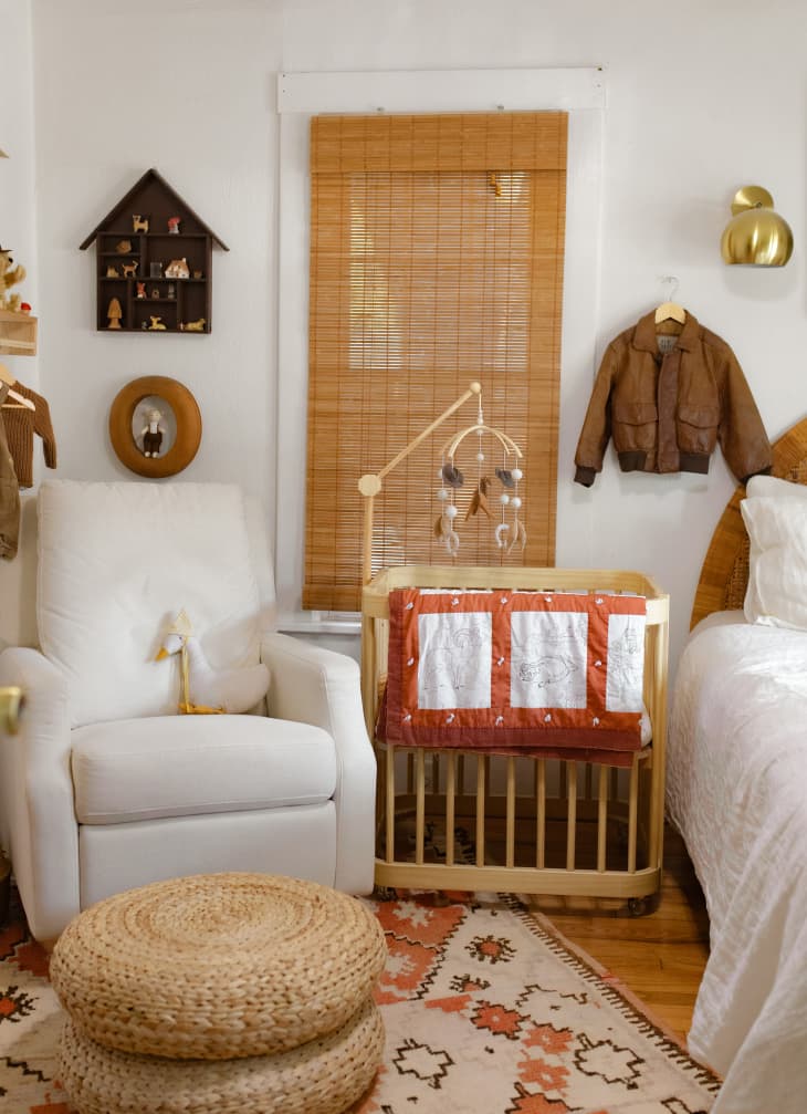 white bedroom with wood bassinet/crib and white armchair with lots of warm hued and natural fiber accents