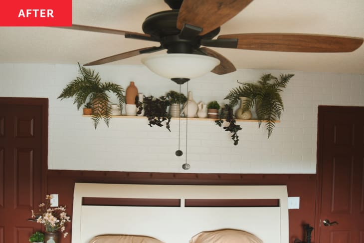 Bedroom with burnt sienna or rust colored walls with floral accent wallpaper and warm decor accents. White painted brick wall over headboard with floating plant shelf