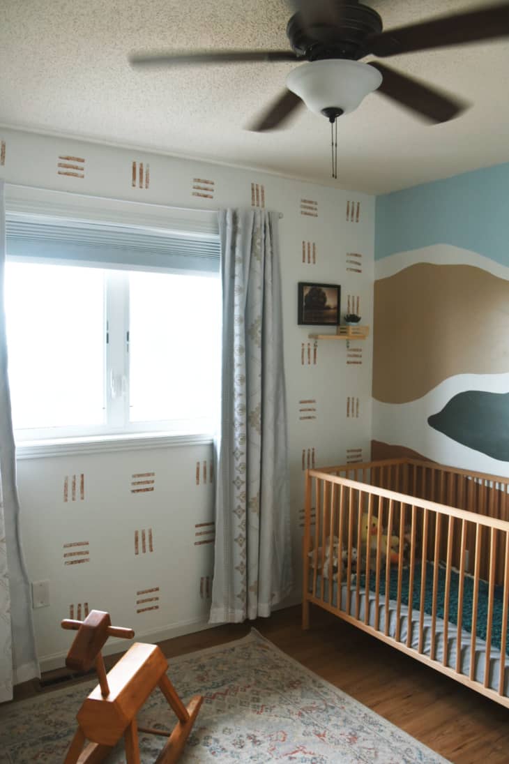 White nursery with gold, blue and green paint and wallpaper design and wood crib