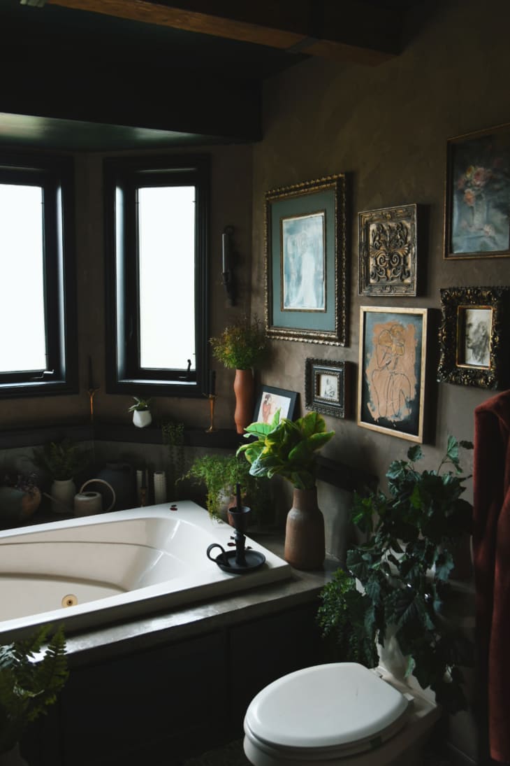 Bohemian brown and dark green bathroom with large bath, plants, lots of windows, gallery wall, and black accents