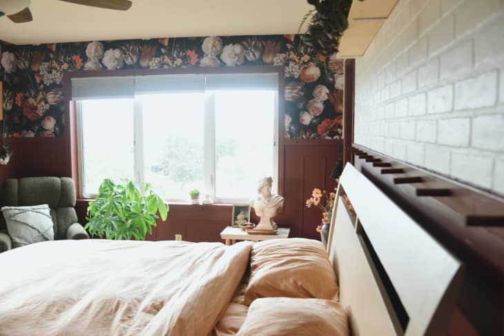 Bedroom with burnt sienna or rust colored walls with floral accent wallpaper and warm accents. White painted brick wall over headboard