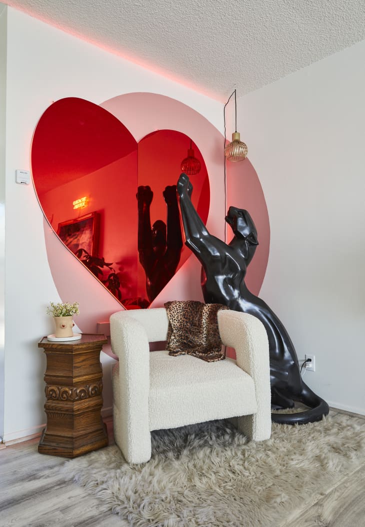 Corner of living room with off white fuzzy chair, large red heart mirror decoration, and black panther sculpture