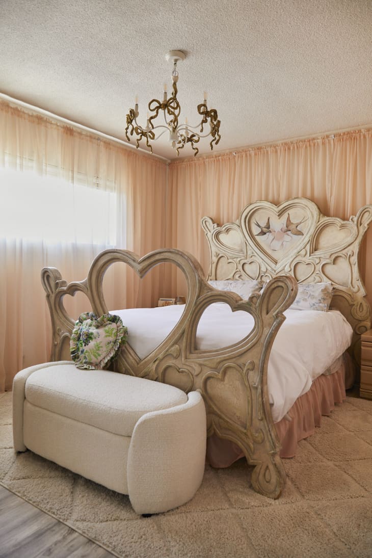 bedroom with peach sheer curtains on all the walls, a decorative carved bed with hearts and birds, and a lyrical bow chandelier