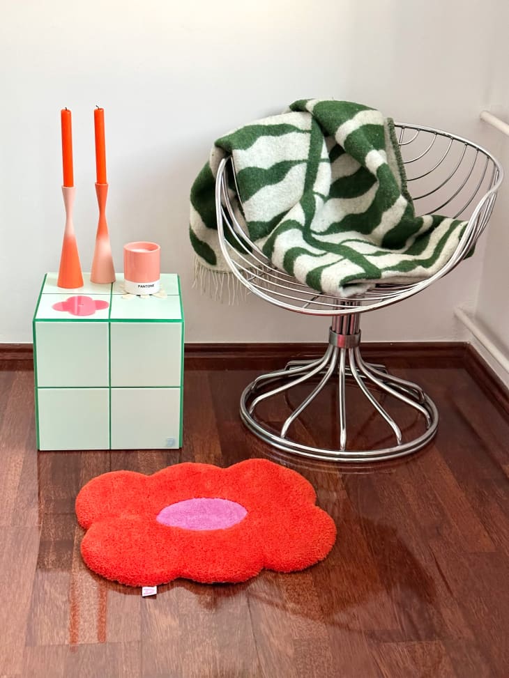 A metal chair next to a tile cube with a candle holder and red/pink rug.