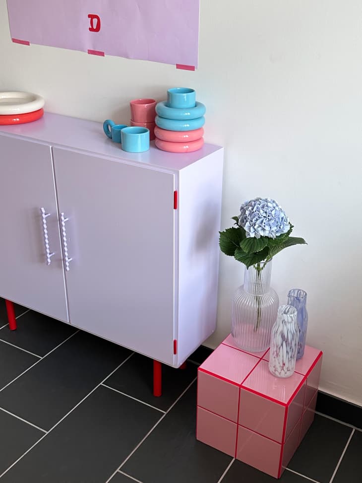 A vase on top of a pink tile cube next to a purple cabinet