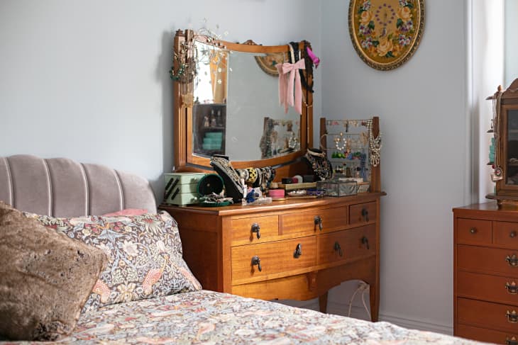A bed with floral sheets and wooden bedroom furniture with decorative items on the wall