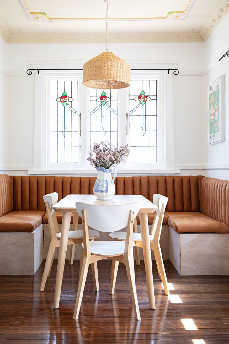 A breakfast nook surrounds a dining table with three chairs in a white kitchen with decorative wall dressings.