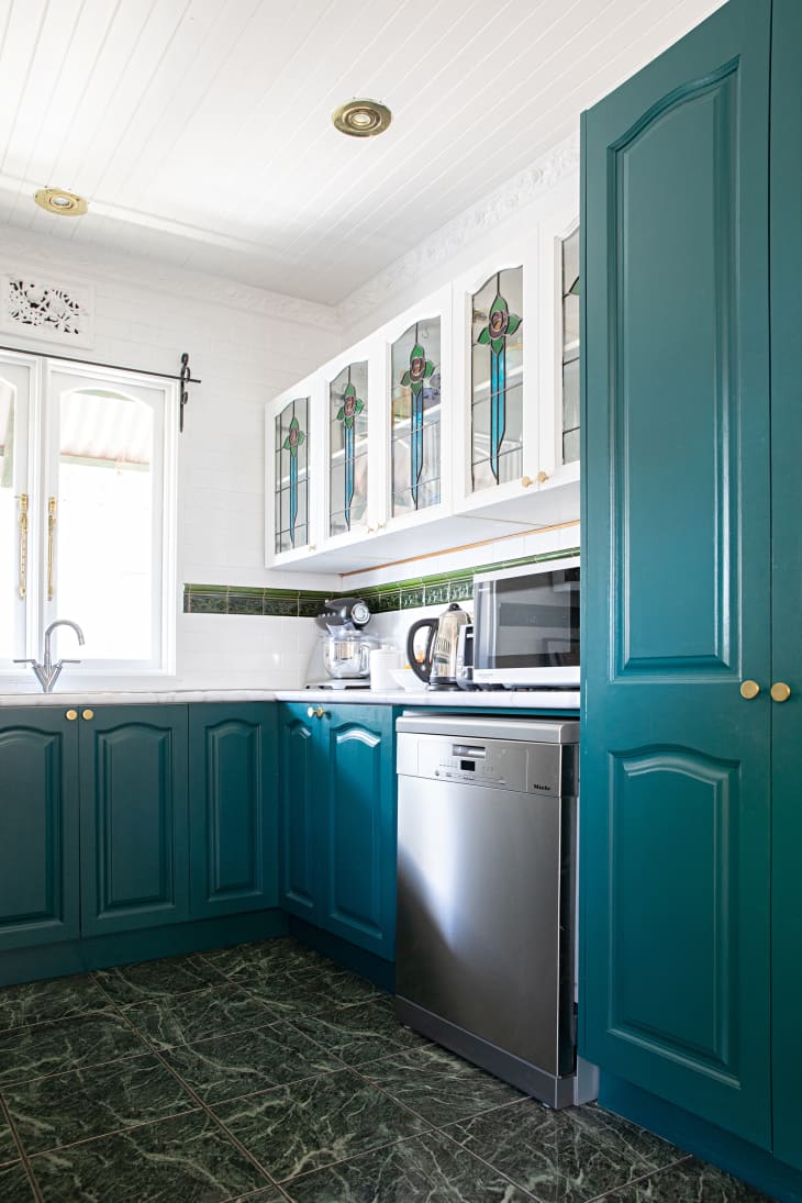 Blue cabinets in a white kitchen with stained glass cabinets.