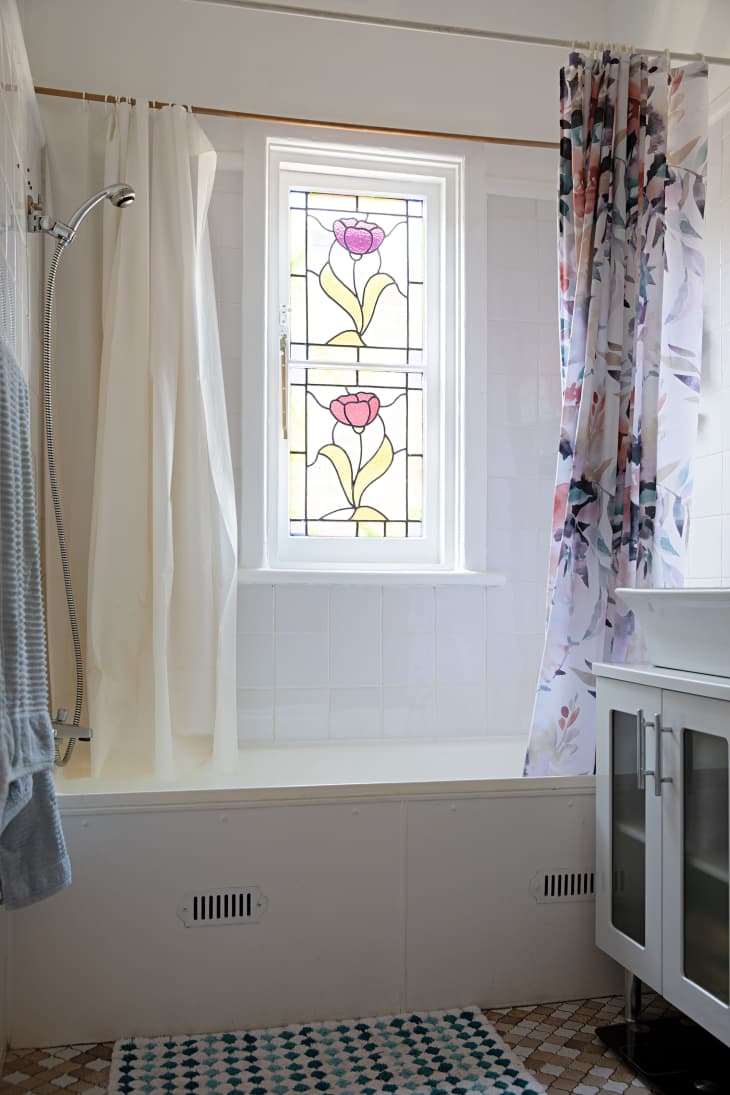 A stained glass window in a white tiled bathroom shower.