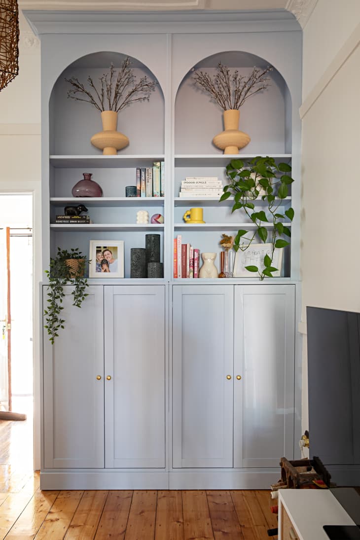 A light blue built-in bookshelf filled with decorative pieces and cabinets in a white living room.