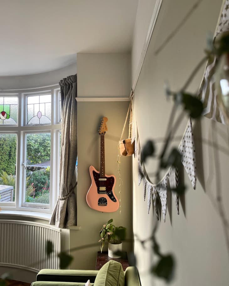 flag banner and green couch arm, guitar hanging on wall next to curved bay windows with stained glass detail, wall trim near ceiling