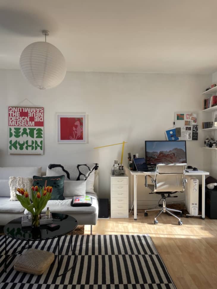 white living area of studio apartment with white sofa, black and white striped rug, and white desk/workspace
