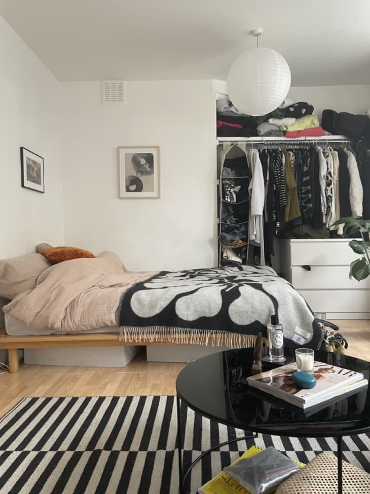 white bedroom area of studio apartment with open plan closet and platform bed with storage underneath