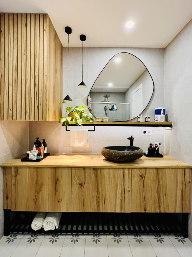 natural wood built in vanity with bowl sink and funky shaped round mirror