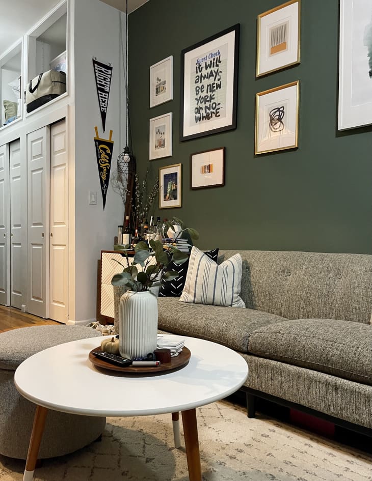 Green living room with gray sofa, white round coffee table, gallery wall, and view into hallway/closet area