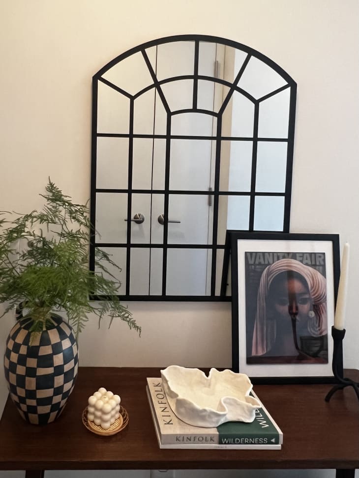 arched window like paneled mirror above dark wood table with checkered vase and artwork on table