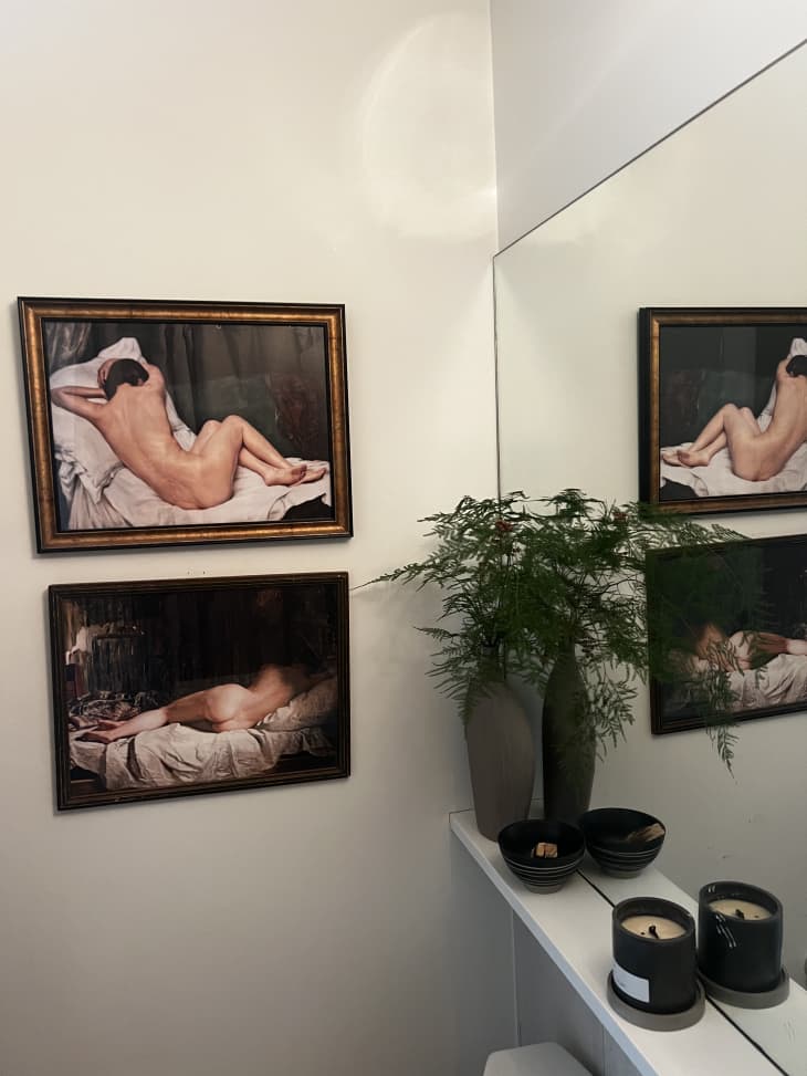 naked portrait artwork hanging in bathroom reflected in mirror with floating shelf below mirror