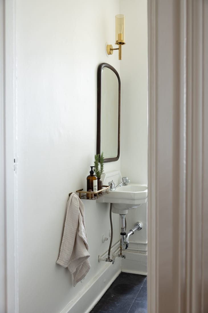 white bathroom with small gold wall sconce over sink mirror