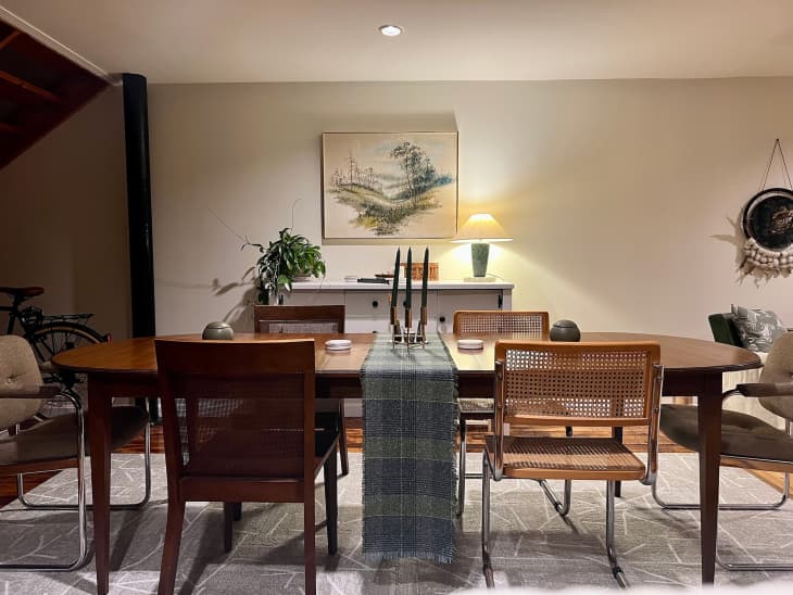 Landscape painting hangs in dining room with wooden oval dining table.