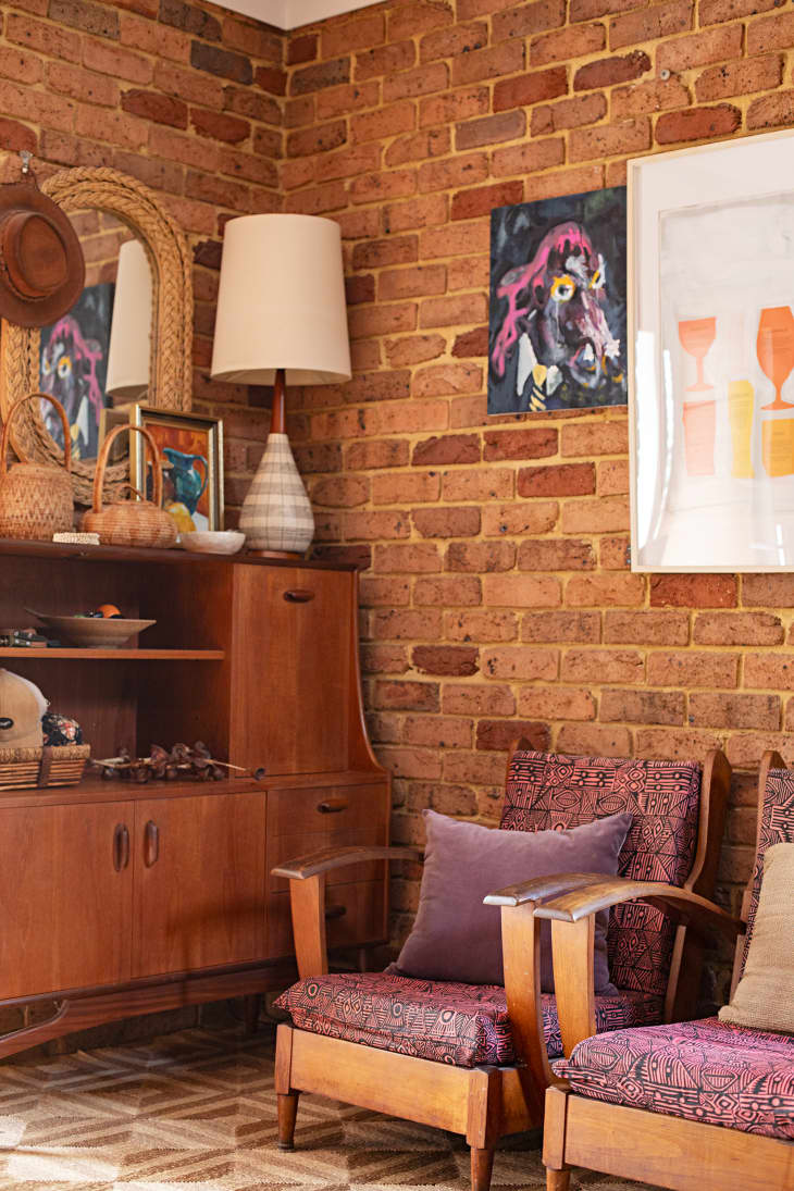Colorful textile print on wooden framed armchair in brick walled room.