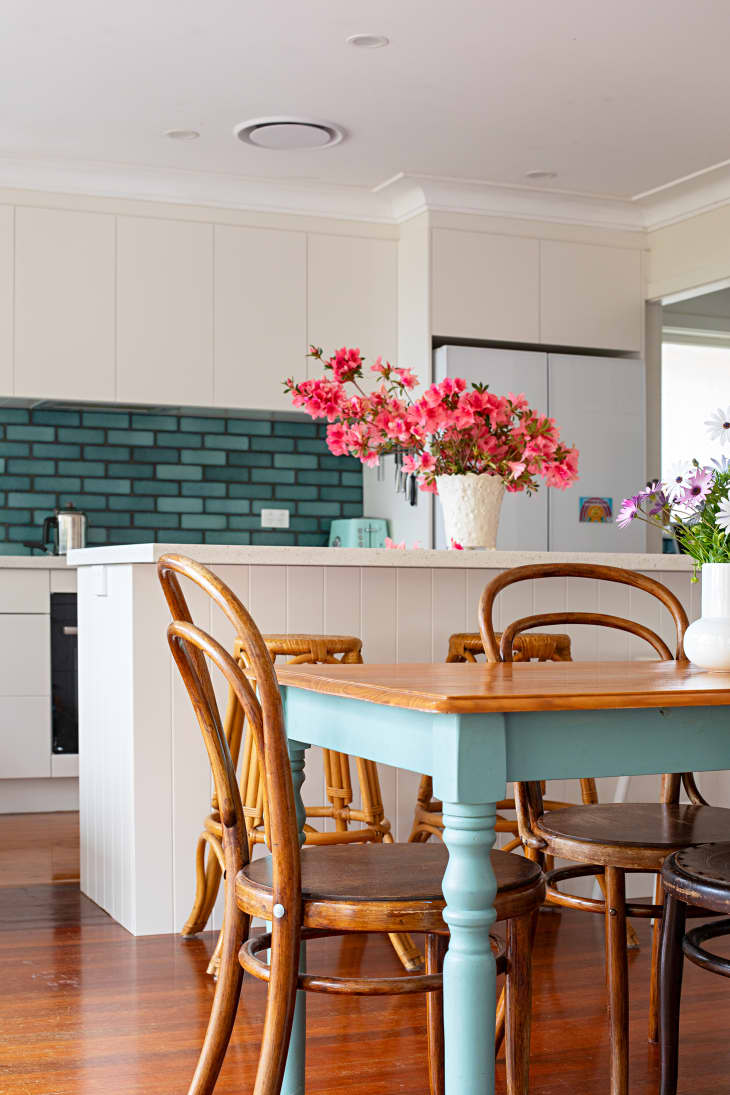 White dining room with aqua and wood table and wood floors. White kitchen island with pink flowers in the background
