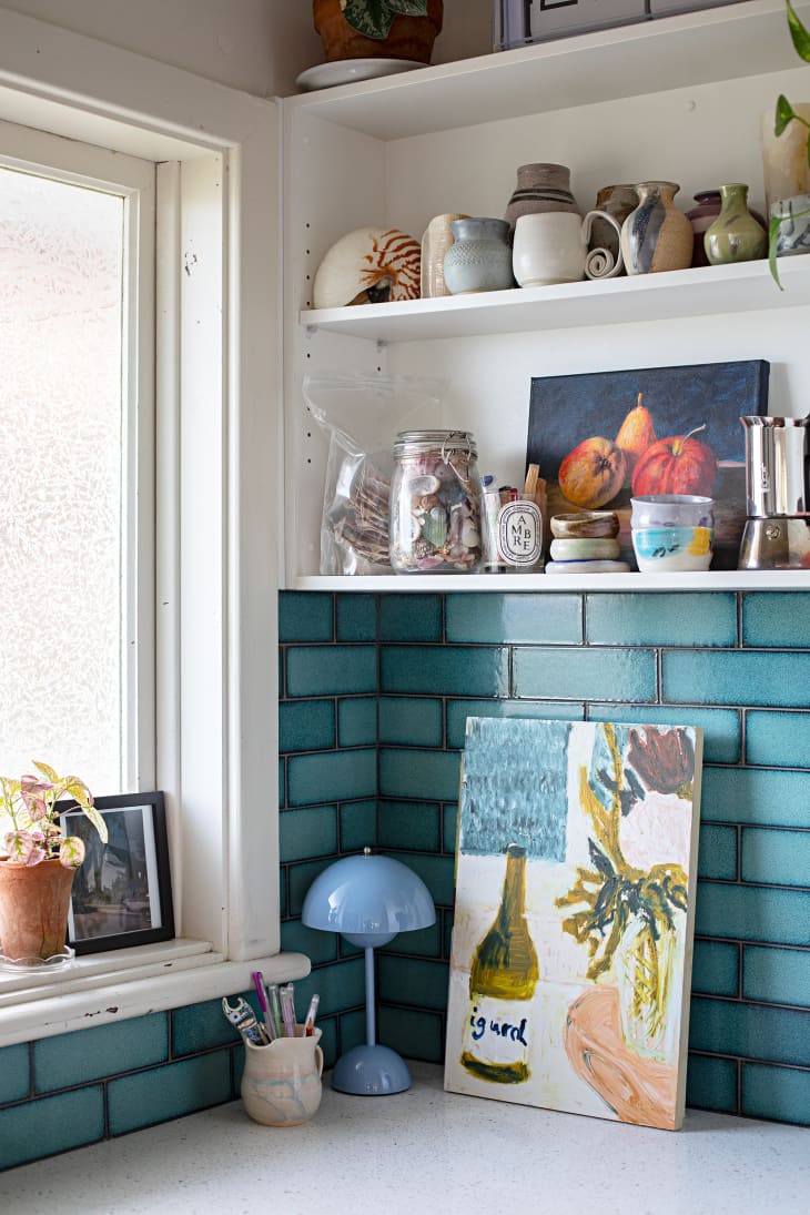 Corner of kitchen counter with blue tile backsplash and open white shelves