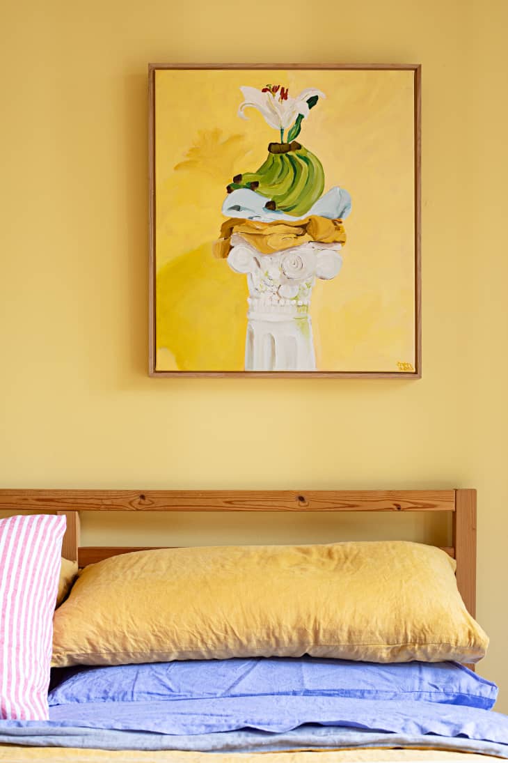 detail of art above wood framed bed in yellow bedroom