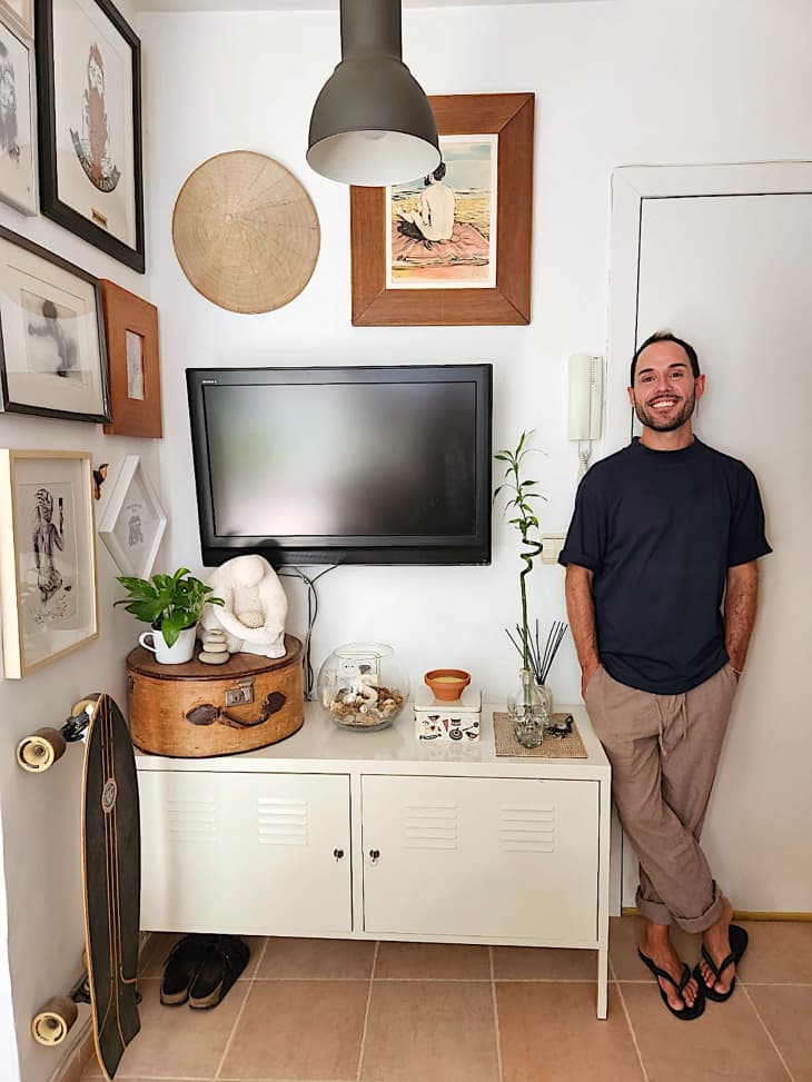 Dweller standing near art filled wall and media center in studio apartment.