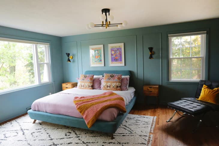 Green painted bedroom with colorfully made bed.