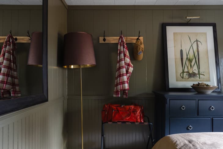 A brass lamp next to the hanging rack and a blue cabinet with framed art on top.