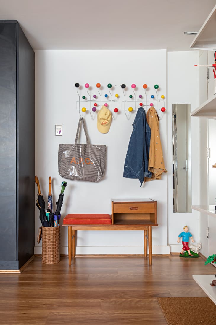 White entryway area with colorful hooks for coats and hats and a wood bench