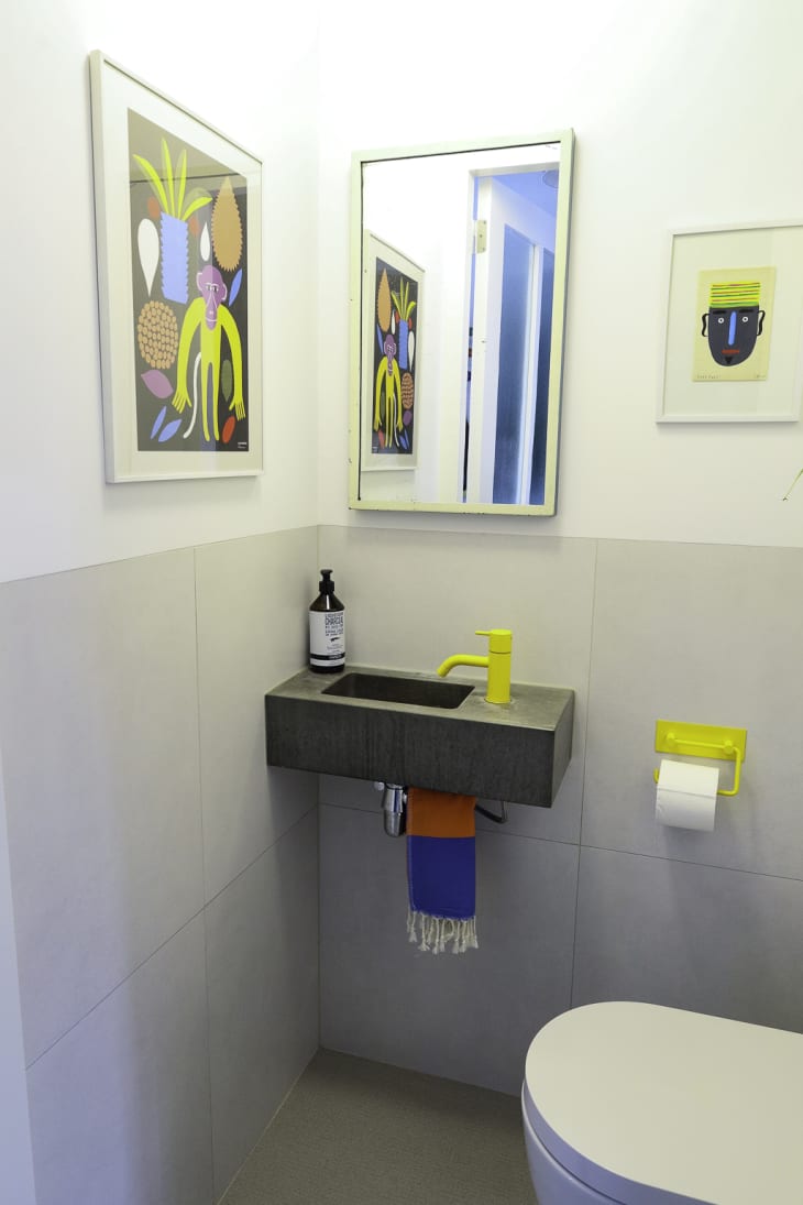 A bathroom with a concrete sink with a yellow faucet and mirror.