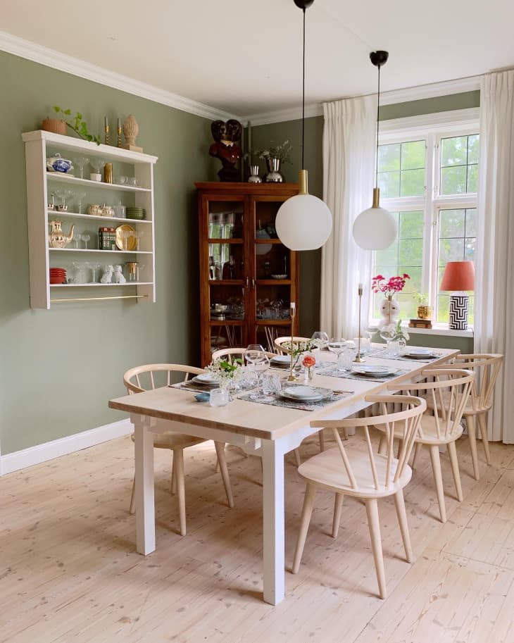 green dining room with a large wooden hutch, large dining table, and globe pendant lamps