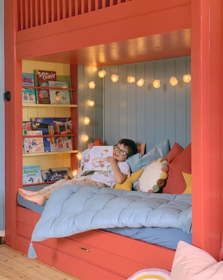 Kids room with coral hideout bunk bed with yellow and blue walls and nestled in bookshelves. Kid on bed