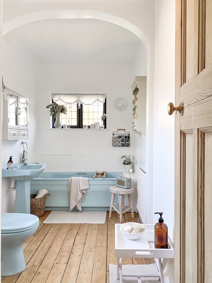 white bathroom with arched doorway, light blue bathtub, sink, and toilet, and wood floor