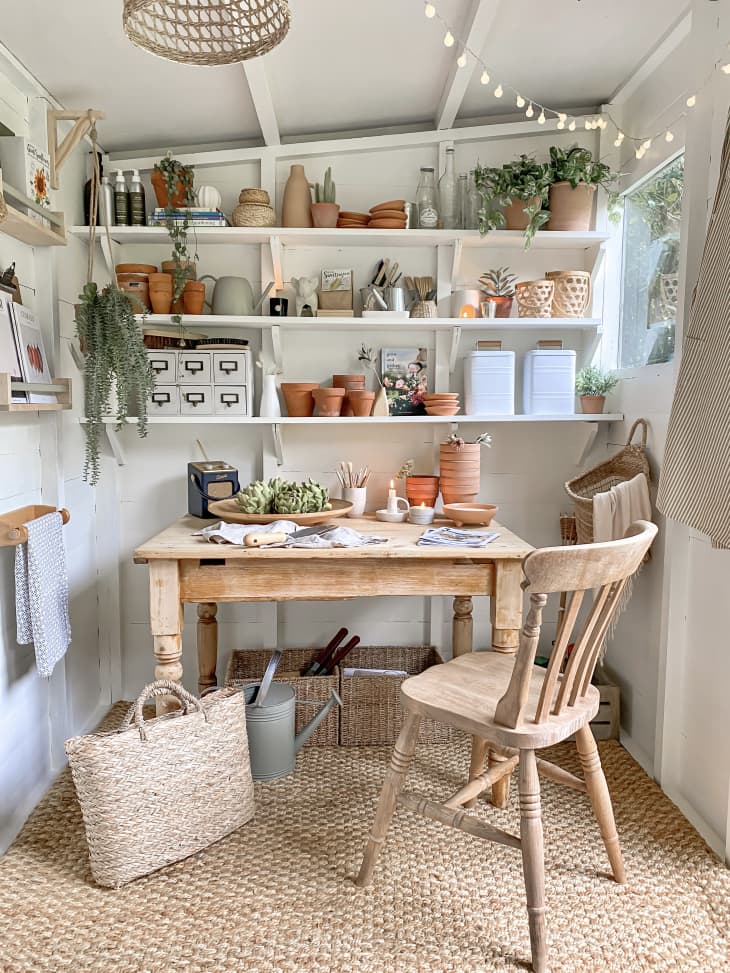 White home workspace area  with rustic wood desk and chair, sisal rug, and lots of plants in terracotta pots