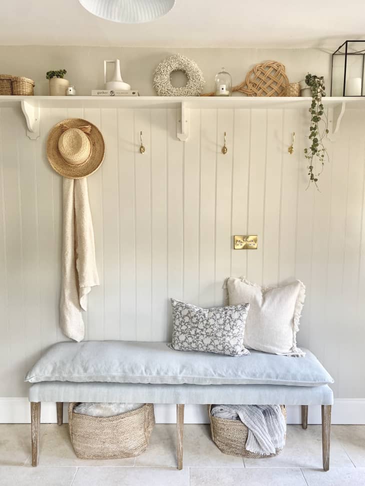 white shiplap hallway with a padded bench and overhead shelf with decorative items.
