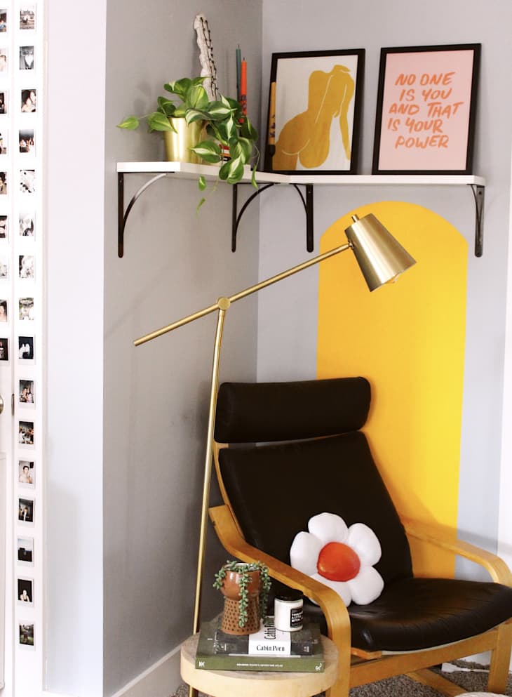 corner of room with yellow paint detail on wall, corner shelf, and black midcentury modern style chair