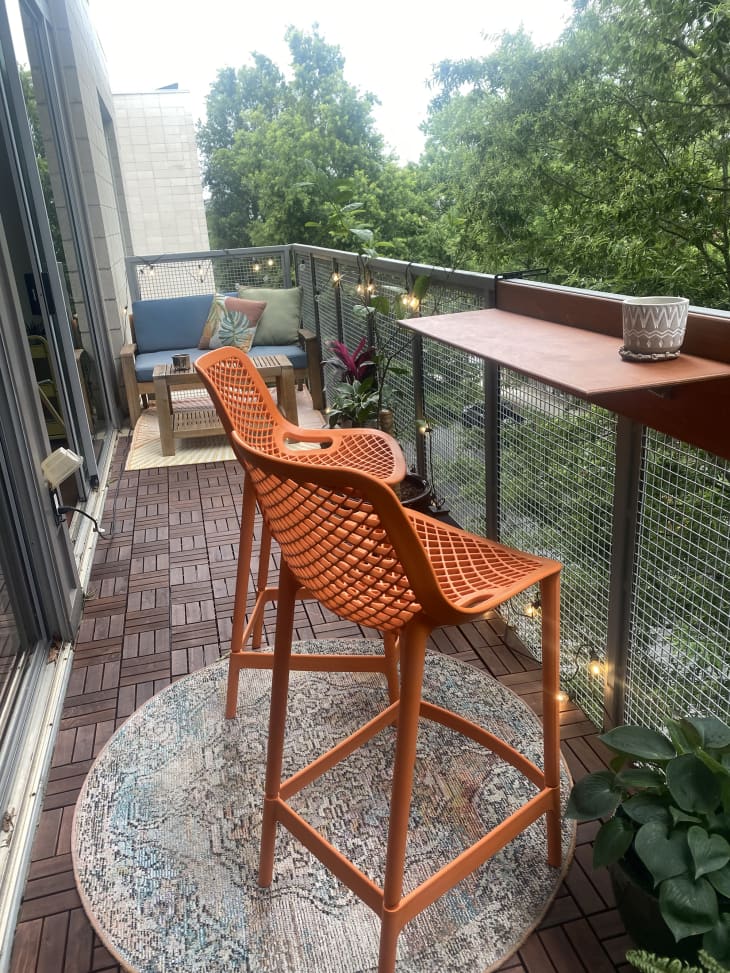 Apartment balcony with orange barstools and ledge table with blue loveseat and coffee table in background