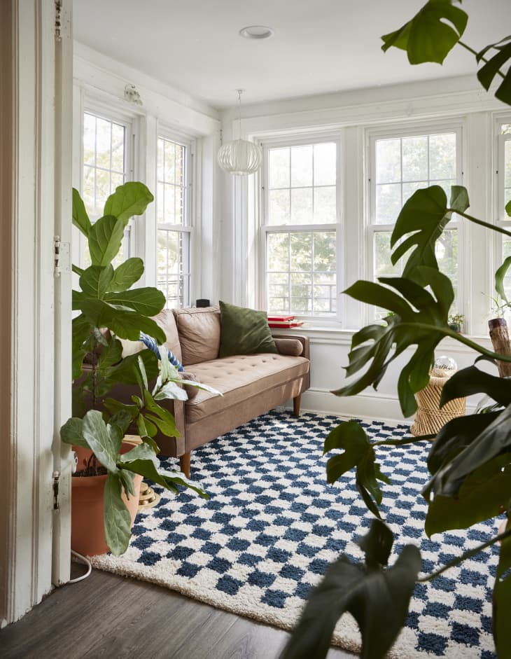 White sunroom with lots of windows, blue and white checked shag rug, and pale brown sofa