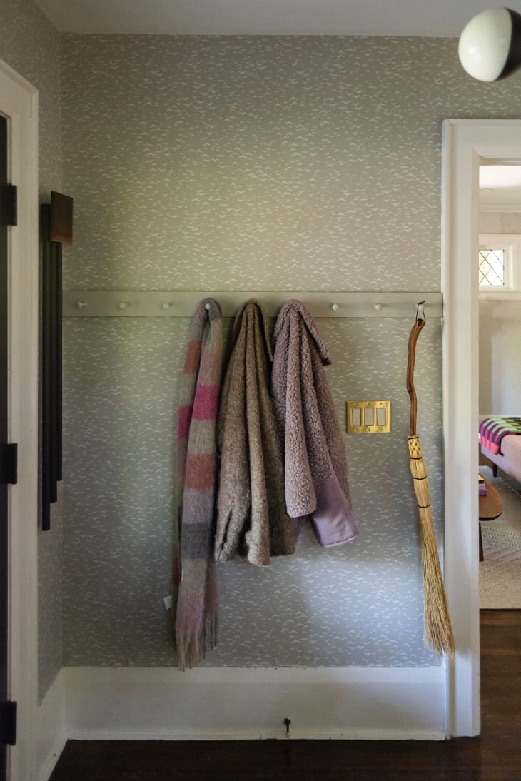 entryway with green patterned wallpaper and hooks for coats, broom
