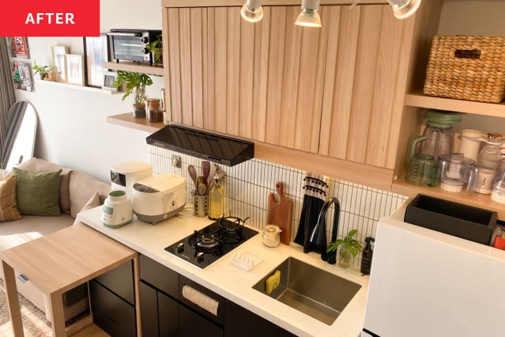 Kitchen after remodel with black lower cabinets with folding island and natural light wood upper cabinets, white countertops, track lighting