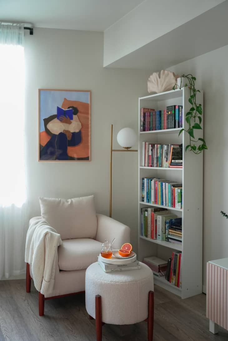 A reading nook in a corner of the living room with a chair, ottoman, and bookshelf.