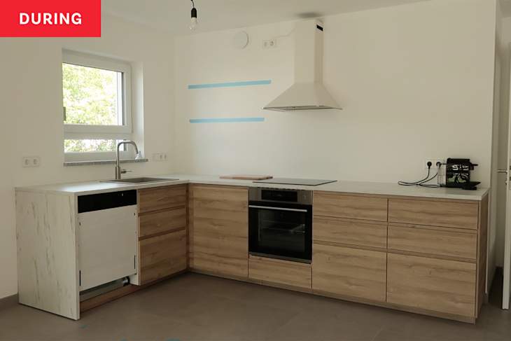 Kitchen during renovation with light wood cabinets and blue tape marking floating shelves