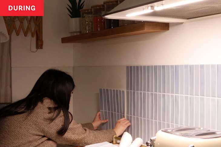 Brunette woman sticking up renter-friendly light blue tiles to make a kitchen backsplash